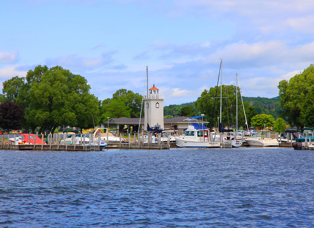 Boyne City, MI - Scenic View of a Lighthouse Surrounded by Green Trees by the Harbor Dock with Boats in Boyne City Michigan