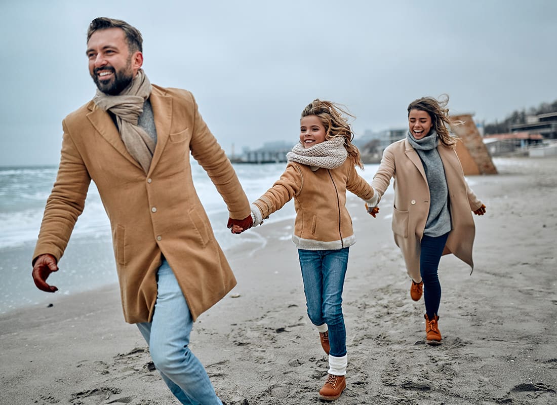 Personal Insurance - View of a Cheerful Family with a Teenage Daughter Having Fun Running on the Sand on the Beach on a Cloudy Winter Day